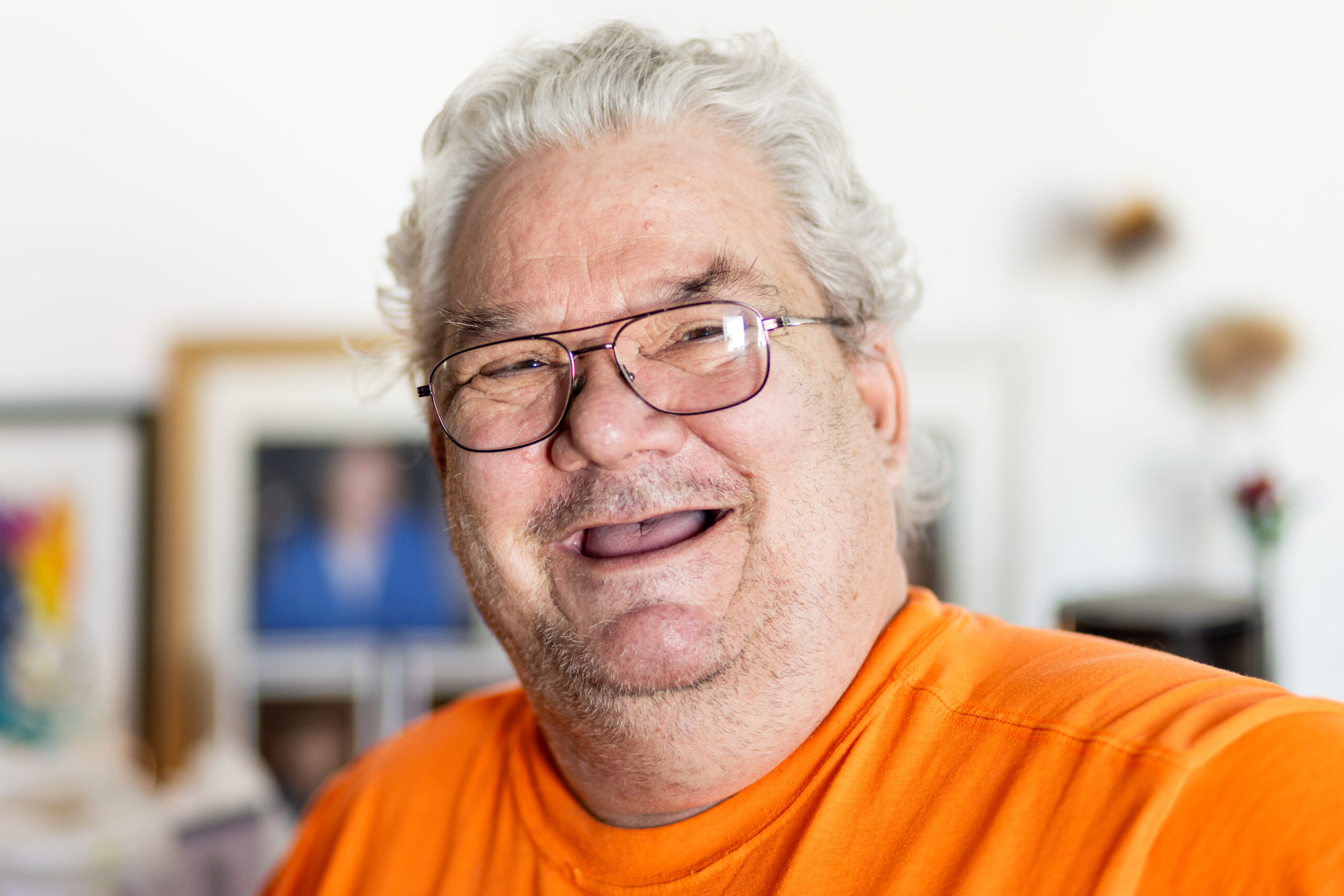 A man with white hair and glasses wearing an orange shirt.