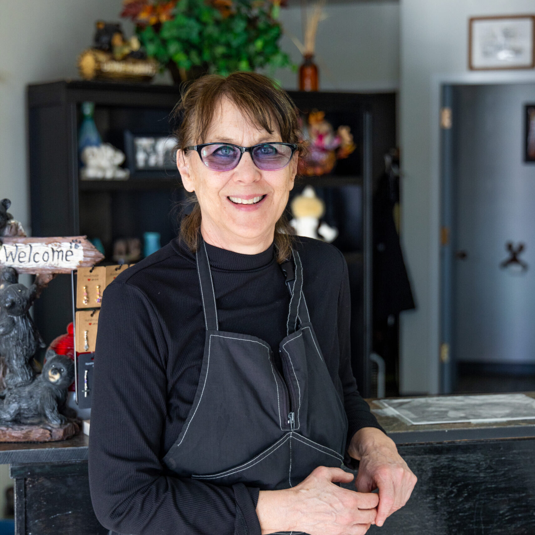 A woman wearing an apron and sunglasses standing in front of a counter.